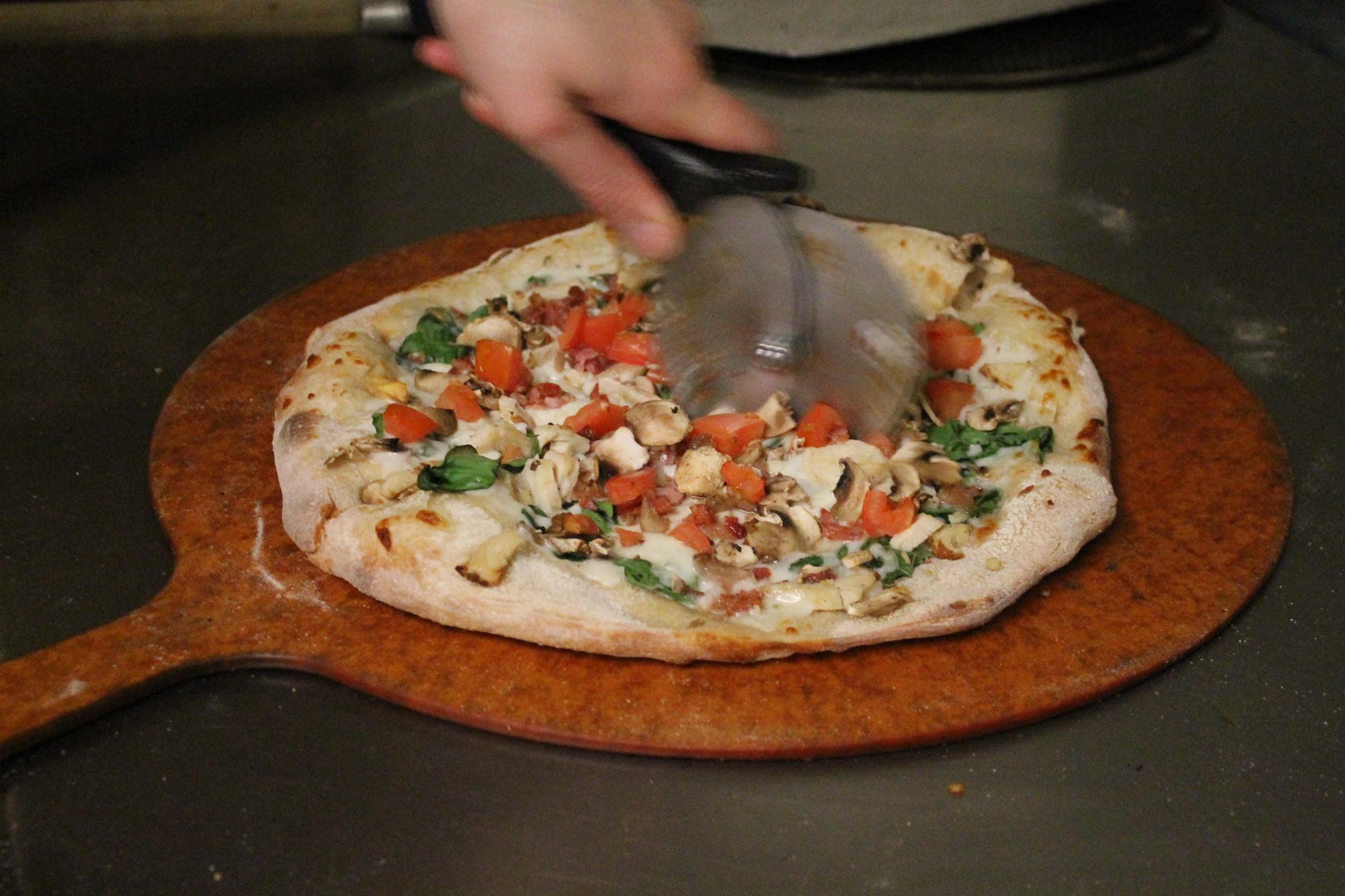 A cook slicing a fresh pizza