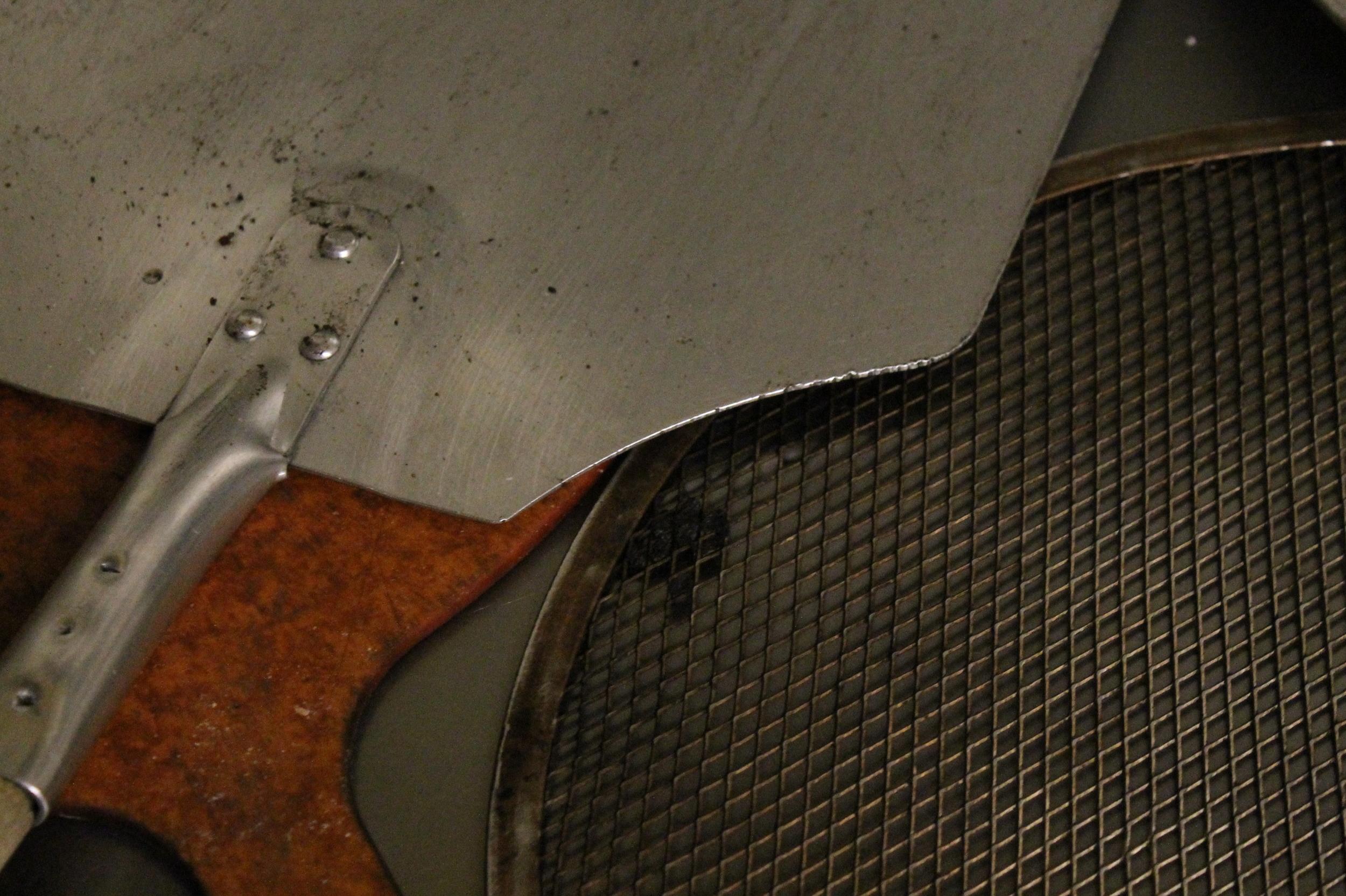 A pizza peel beside a well-used pizza screen